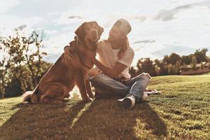 Handsome young man and his dog sitting on the green lane while spending time outdoors photo