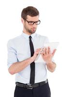 Businessman with digital tablet. Cheerful young man in formalwear and glasses working on digital tablet while standing isolated on white background photo