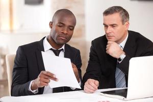 Discussing a project. Two confident business people in formalwear discussing something while one of them pointing a paper photo