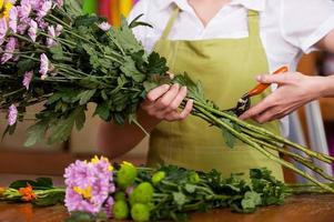 Florist at work. Cropped image of female florist in apron cutting flowers photo