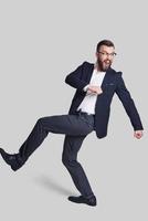 On the way... Full length of handsome young man in formalwear making a face and gesturing while walking against grey background photo