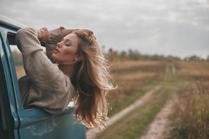 On the way to unknown places. Attractive young woman leaning out the vans window and keeping hand in hair while enjoying the car travel photo