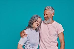 Happy senior couple smiling while standing together against blue background photo