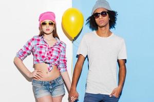 They are cool Funky young couple holding yellow balloon and looking at camera while standing against colorful background photo