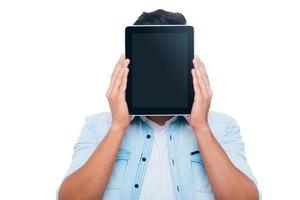 Tablet face. Young man hiding his face behind digital tablet while standing against white background photo