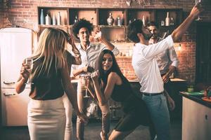 Playing hard. Cheerful young people dancing and drinking while enjoying home party on the kitchen photo