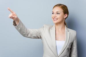 Look over there Smiling young businesswoman pointing away while standing against grey background photo