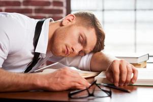 autor dormido. apuesto joven con camisa y corbata durmiendo mientras está sentado en el escritorio foto