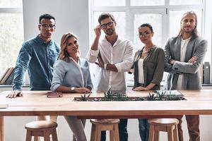 logrando mejores resultados juntos. grupo de jóvenes modernos con ropa informal inteligente mirando la cámara y sonriendo mientras trabajan en la oficina creativa foto