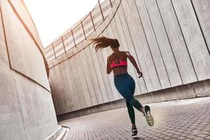 logrando mejores resultados. vista trasera completa de una mujer joven con ropa deportiva trotando mientras hace ejercicio al aire libre foto