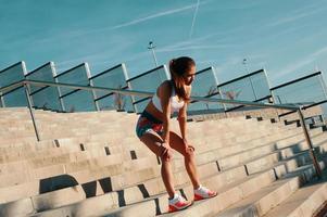 Time to rest. Full length of beautiful young woman in sports clothing relaxing while exercising outdoors photo