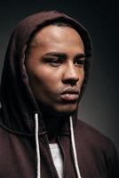 Confidence and concentration. Confident young African man in hooded shirt looking away while standing against grey background photo