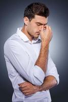 Lost in thoughts. Side view of handsome young man in white shirt holding hand in hair and looking away while standing against grey background photo