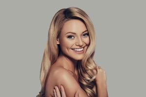 Her confidence shines through. Attractive young woman with long curly blond hair smiling and looking at camera while standing against grey background photo