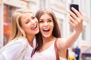 Friends making selfie. Two beautiful young women making selfie and grimacing photo