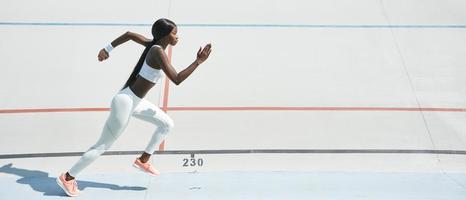 confiada joven africana en ropa deportiva corriendo en la pista al aire libre foto