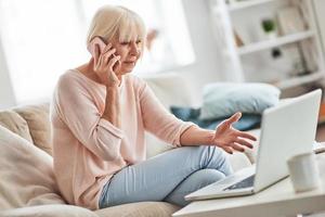 Discussing something important. Beautiful senior woman talking on her smart phone and gesturing while relaxing on the couch at home photo