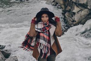 In her own style. Attractive young woman covered with blanket looking at camera while standing near the river in mountains photo