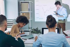 Group of young modern people in smart casual wear analyzing data on projection screen in the office photo