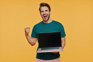 Handsome young smiling man in casual clothing carrying laptop and gesturing photo