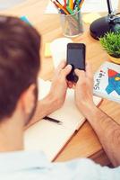 Typing business message. Close-up of man holding his mobile phone upon wooden table photo