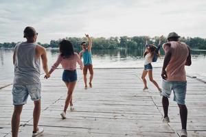 totalmente libre. grupo de jóvenes con ropa informal sonriendo y gesticulando mientras corren en el muelle foto