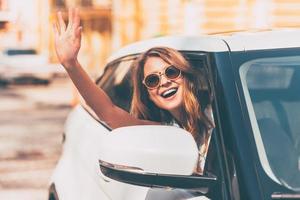 Hello Beautiful young cheerful women looking at camera with smile and waving while sitting in her car photo
