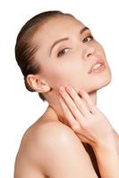 Pure beauty. Side view of beautiful young shirtless woman touching her cheek and looking at camera while isolated on white background photo