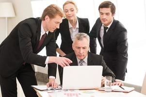 Business discussion. Four business people in formalwear discussing something while one of them pointing laptop photo