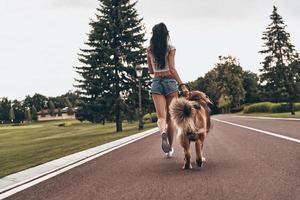 Full length rear view of young woman running with her dog through the park while spending time outdoors photo