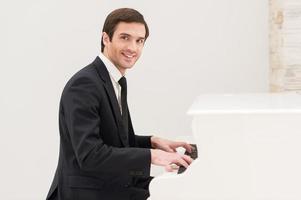 Piano man. Cheerful young man in formalwear playing piano and looking at camera photo