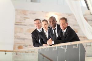 equipo de negocios confiado. vista de ángulo bajo de cuatro empresarios confiados parados uno cerca del otro y sonriendo a la cámara foto