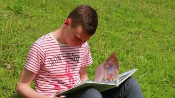 menino lendo um livro sobre a natureza, sentado na grama verde video