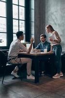 Group of young cheerful people in smart casual wear discussing something while working in office photo