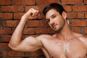 Masculinity. Handsome young muscular man posing while standing against brick wall photo