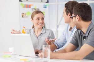 Brainstorming. Three young colleagues sitting together at their working place while woman telling something and gesturing photo
