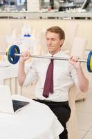 I choose healthy lifestyle. Smiling young red hair man in shirt and tie sitting at the restaurant and holding a dumbbell photo