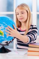 Examining globe. Cheerful little girl examining globe while sitting at the table photo