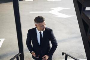 Top view of confident mature businessman carrying mobile phone while walking outdoors photo