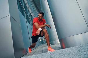 Charming young man in sports clothing making a lunge and stretching while exercising outdoors photo