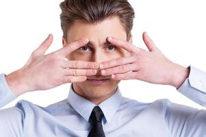 Looking through fingers. Portrait of confident young man in formalwear looking at camera through the fingers  while standing isolated on white photo