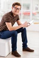 Man with digital tablet. Side view of handsome young man working on digital tablet and looking at camera photo