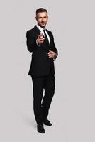 You are the one I need Full length of handsome young man in full suit pointing you and looking at camera with smile while standing against grey background photo