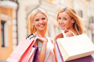 siempre vamos de compras juntos. alegre mujer madura y su hija cargando bolsas de compras y mirando la cámara mientras caminan al aire libre foto