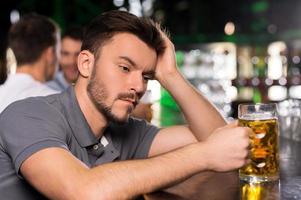 It was a hard day. Depressed young man drinking beer in bar and holding hand in hair photo