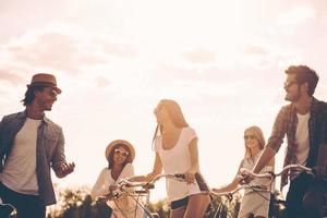 Carefree talk with friends. Low angle view of cheerful young people talking while standing near their bicycles on the road photo