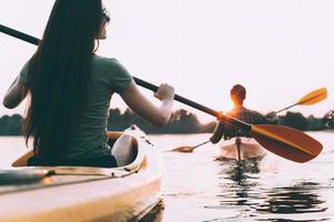 Couple kayaking. Rear view of beautiful young couple kayaking on river together with sunset in the background photo