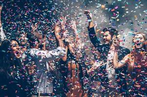 Confetti fun. Group of beautiful young people throwing colorful confetti while dancing and looking happy photo