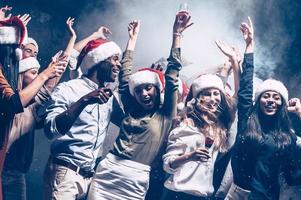 Enjoying New Year party. Group of beautiful young people in Santa hats dancing and looking happy photo