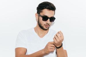 In his own casual style. Handsome young Indian man adjusting his bracelet and looking at camera while standing against white background photo